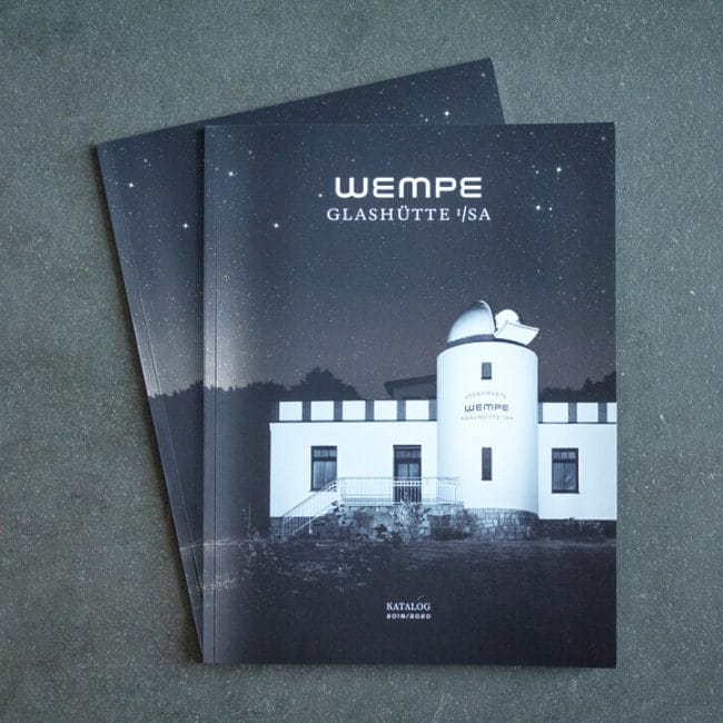 Auf einer grauen Fläche liegen zwei Kataloge mit dem Titelbild eines weißen Sternwartengebäudes unter einem nächtlichen Sternenhimmel mit dem Titel Wempe Glashütte I/SA.